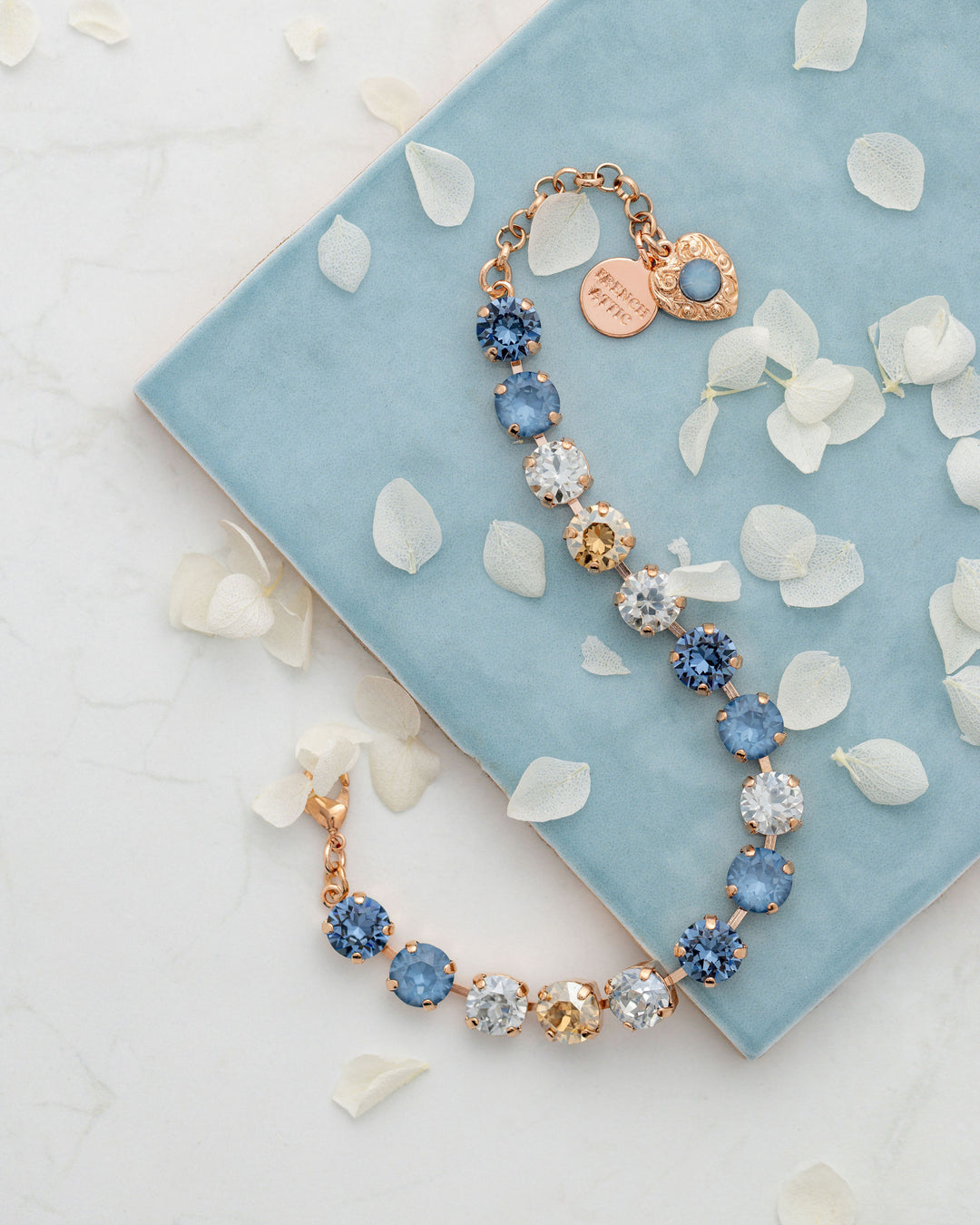 Bracelet with blue and gold crystals on a light blue fabric background with white petals.