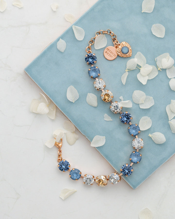 Bracelet with blue and gold crystals on a light blue fabric background with white petals.