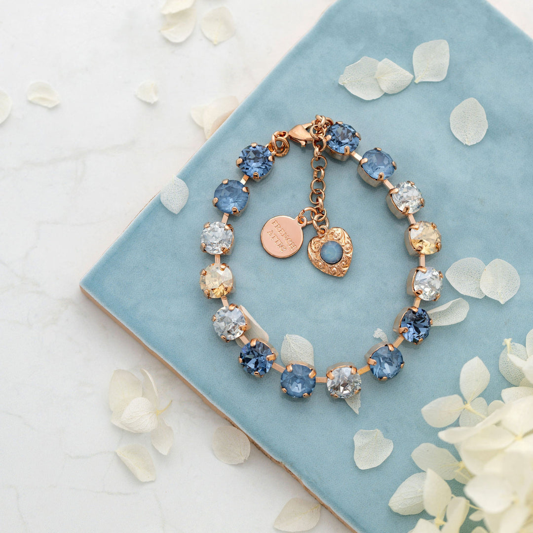 Crystal tennis bracelet with blue and clear stones on a blue background with white petals.