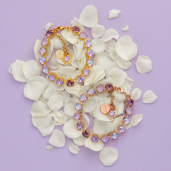 Two tennis bracelets with purple crystals on white flowers against a light purple background
