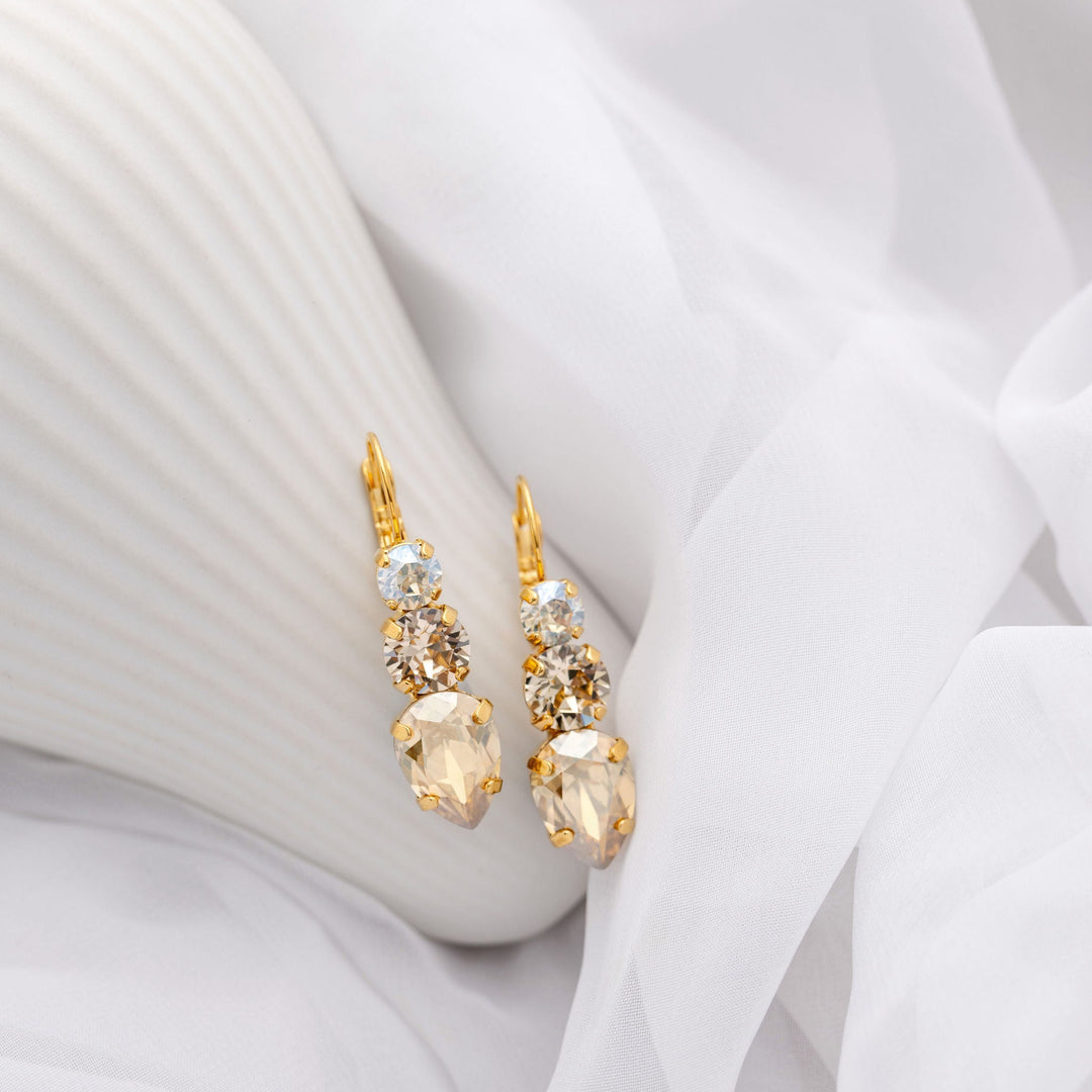 Gold earrings with champagne crystals on a white fabric background