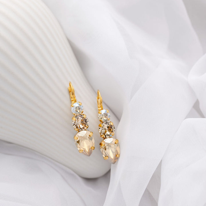 Gold earrings with champagne crystals on a white fabric background