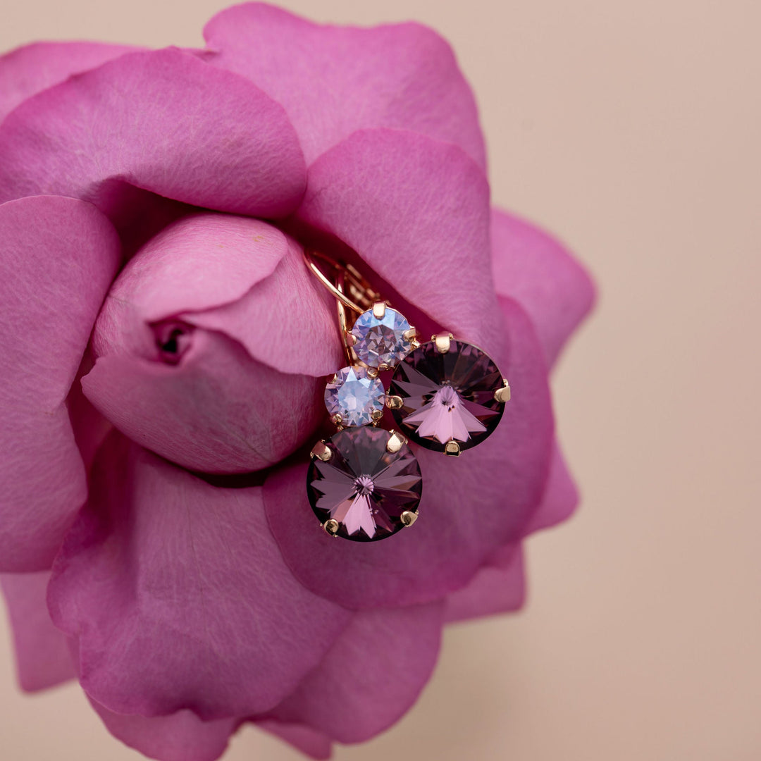 Earrings with dark pink crystals on a pink rose against a beige background