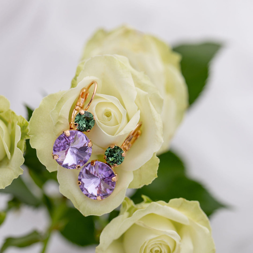 Gold earrings with purple and green crystals on a bed of white roses.